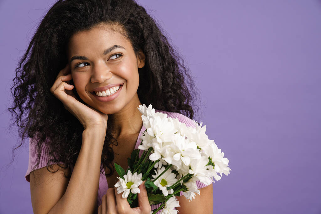 Молода чорна жінка посміхається, позуючи з хризантемою ізольовано на фіолетовому фоні
 - Фото, зображення