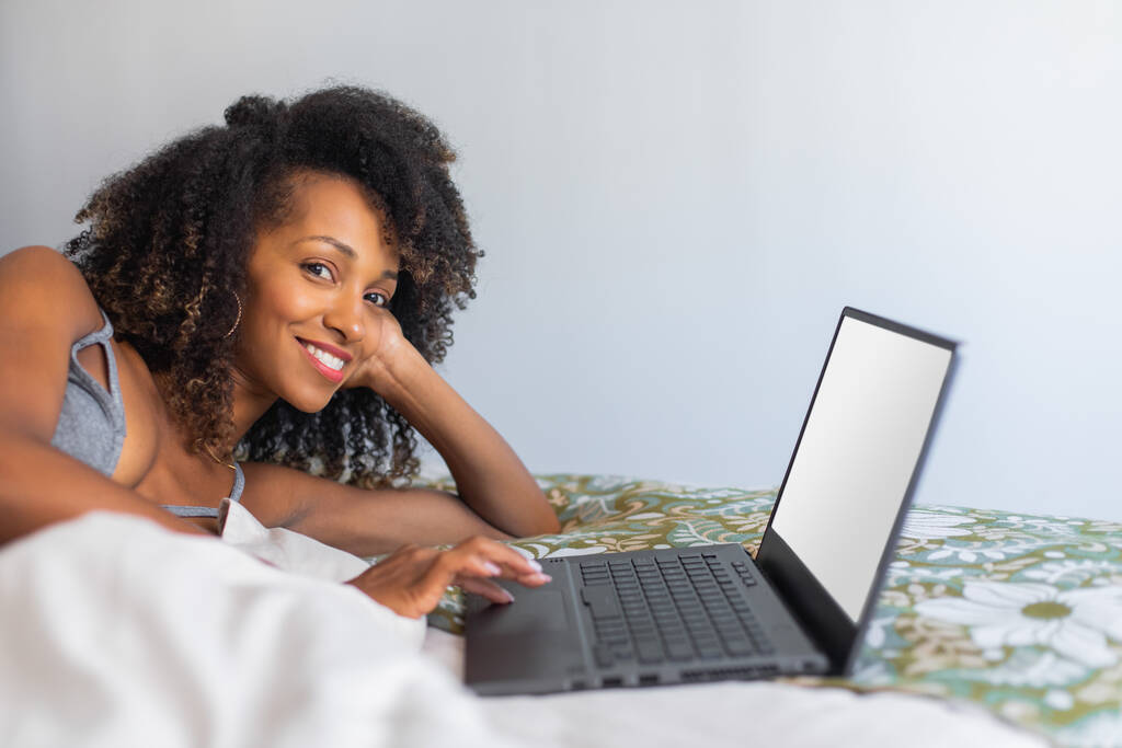 Evdeki yatağında dizüstü bilgisayar kullanan rahat mutlu bir kadın. Boş internet sörfü ve medya tüketimi kavramı. - Fotoğraf, Görsel