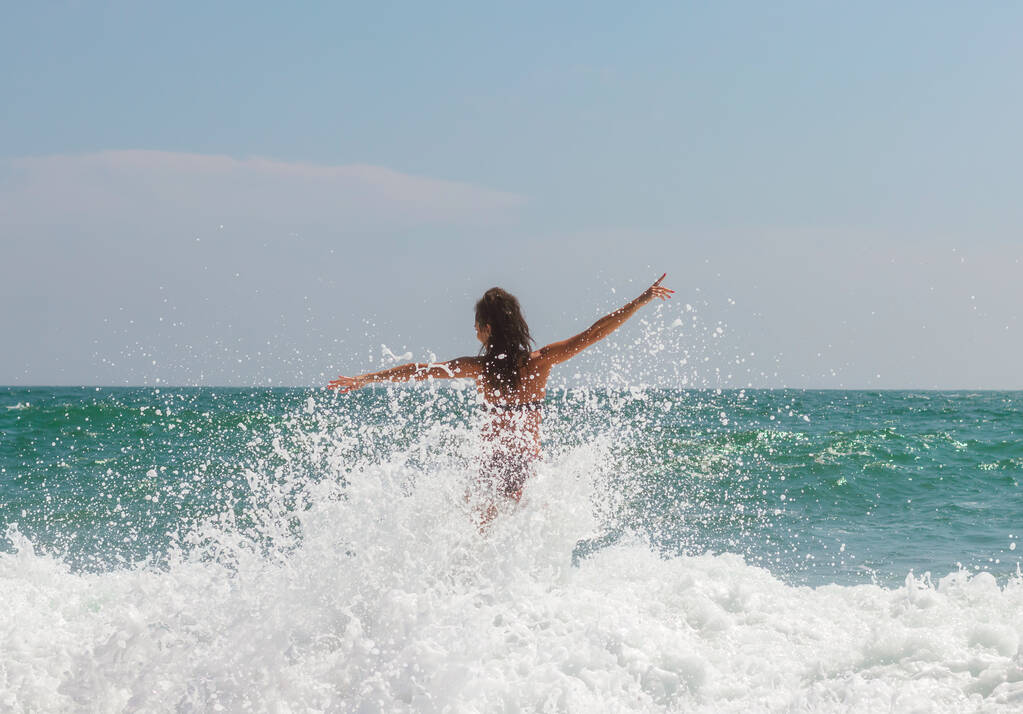 Ein schönes Mädchen genießt die Wellen des Ozeans. Spritzer, viele Tropfen - Foto, Bild