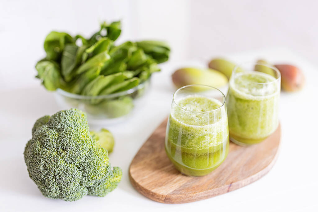 Ingredientes frescos para un cóctel desintoxicante saludable de color verde. Dos vasos con bebida para dieta en plato de madera, al lado brócoli y otras verduras y frutas. - Foto, imagen