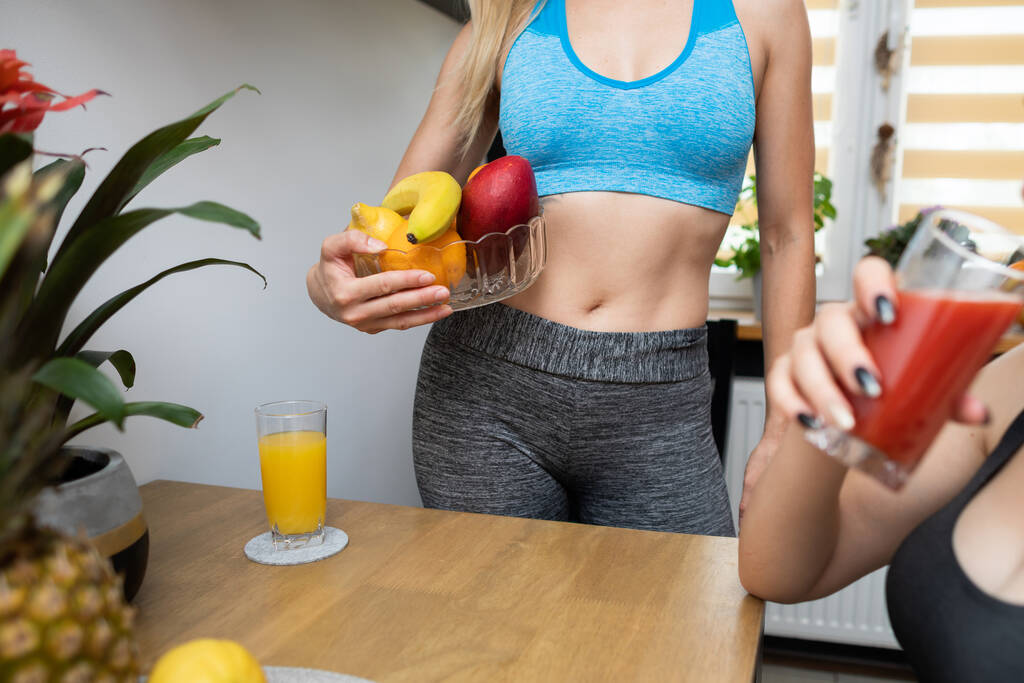 Egy atlétikai lány egy gyümölcskosarat tart a csípőjénél. Egy adag energia edzés előtt. - Fotó, kép