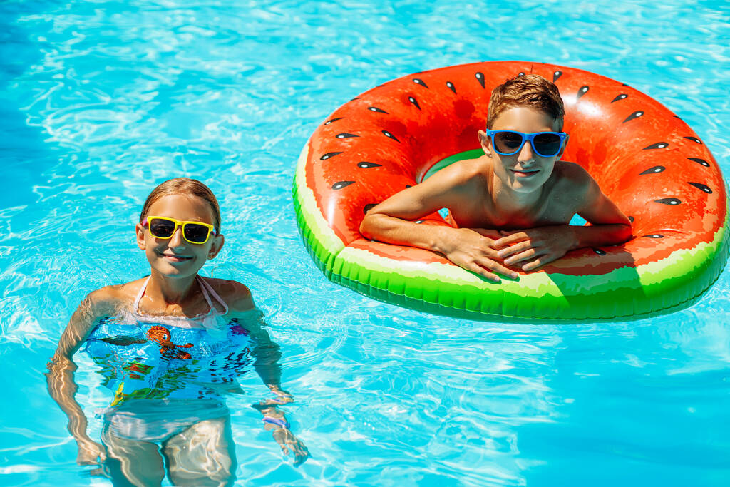 Šťastné děti, chlapec a dívka ve slunečních brýlích, plavat a hrát si s nafukovacími kroužky, bavit se a cákat vodu v krásném bazénu v tropickém letovisku, bavit se během rodinné letní dovolené - Fotografie, Obrázek