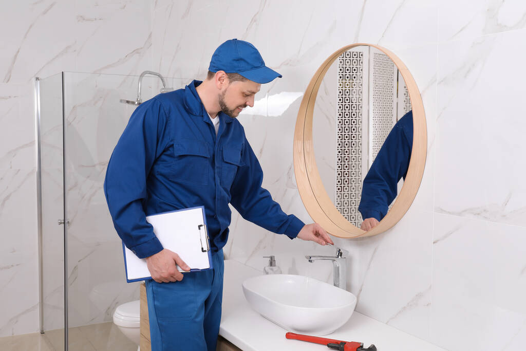 Professioneller Klempner mit Klemmbrett überprüft Wasserhahn im Badezimmer - Foto, Bild