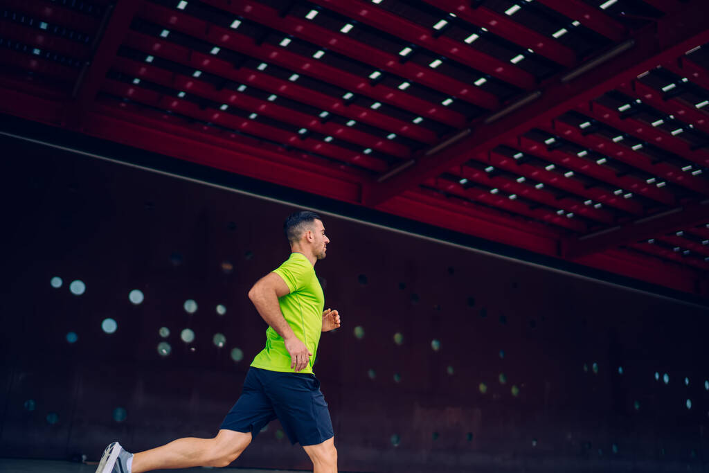 Вид сбоку на бегущего мужчину во время кардиотренировки в городской среде, белый мужчина, наслаждающийся выносливостью во время разминки концентрации на досуге для тренировки физической напряженности - Фото, изображение