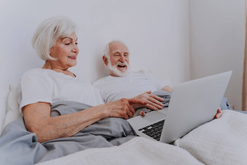 Όμορφο ζευγάρι ηλικιωμένων απολαμβάνει το χρόνο μαζί στο σπίτι - Moder ηλικιωμένο ζευγάρι σερφάροντας στο διαδίκτυο σε φορητό υπολογιστή - Φωτογραφία, εικόνα