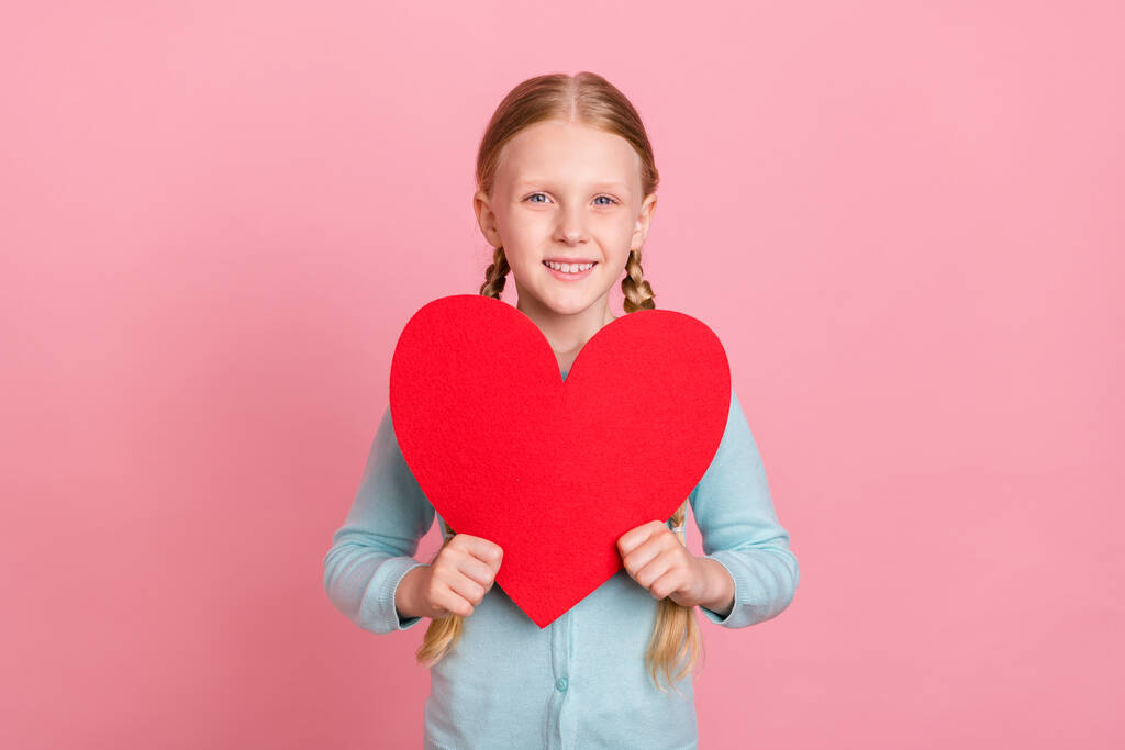 Foto von ziemlich glänzend Schulmädchen tragen blaue Strickjacke hält großes rotes Herz lächelnd isoliert rosa Hintergrund - Foto, Bild