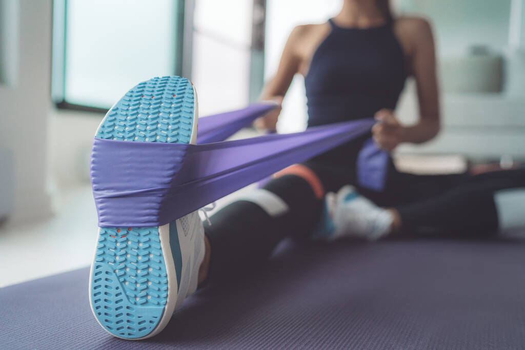Verzetsband oefening thuis. Vrouw doet pilates workout met behulp van elastische riem trekken met armen voor schoudertraining op yoga mat binnen - Foto, afbeelding