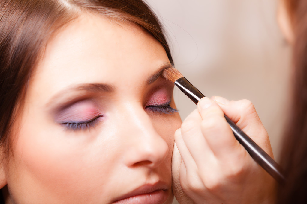 Artista de maquillaje aplicando con cepillo cosmético en la ceja de la mujer
 - Foto, Imagen