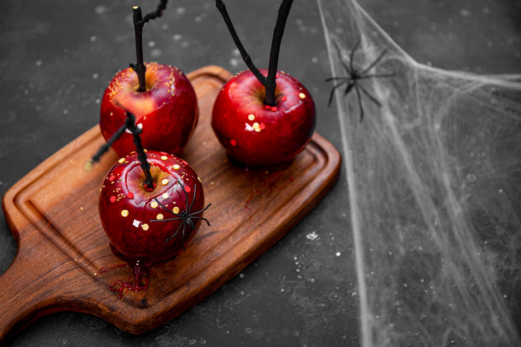  Красные яблоки в карамели с праздничным декором на Хэллоуин, оригинальное угощение праздничного стола на Хэллоуин, украшенного пауками и паутиной, пространство для копирования текста - Фото, изображение