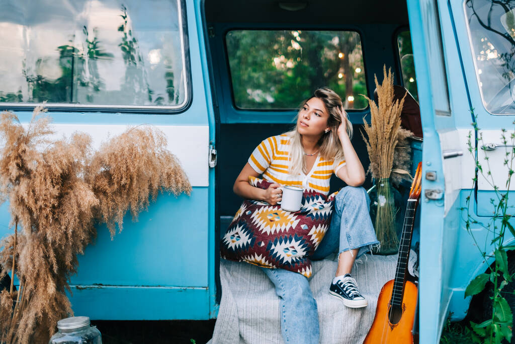 Ritratto di giovane donna felice seduta in un furgone e che beve tè all'aperto nella natura, durante il tramonto. Godersi l'estate, concetto di viaggio - Foto, immagini