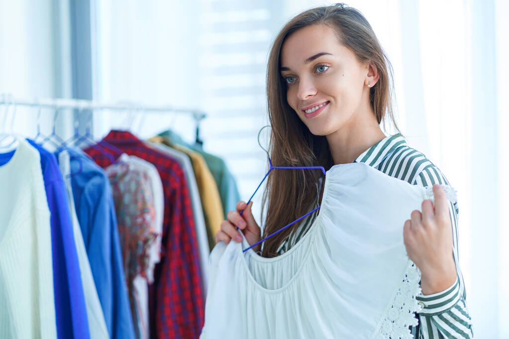 Portrét šťastné roztomilé mladé brunetky žena se snaží moderní módní stylové ženské oblečení během nákupu oblečení v obchodě a výběru oblečení na sebe  - Fotografie, Obrázek