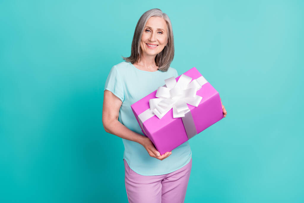 Photo of smiling cheerful nice looking mature woman grandmother hold birthday present isolated on teal color background - Photo, Image