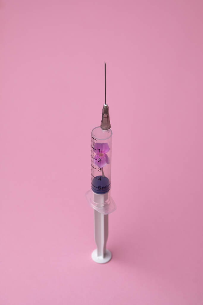 Креативная вакцина против коронавируса на розовом фоне 2019-nCoV или COVID-19. Вспышка коронавируса. Вирус эпидемии респираторного синдрома. Шприц с цветами. Пандемия минимального фона. - Фото, изображение