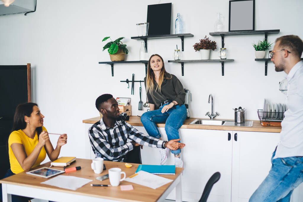 Group of thoughtful multiracial coworkers in casual outfits talking about business ideas while working together in modern light kitchen during meeting - Photo, Image