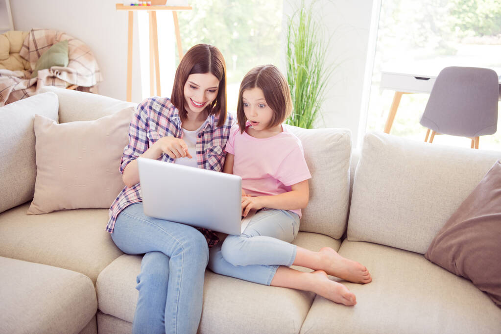 Retrato de duas meninas alegres atraentes sentadas no divã usando laptop se divertindo assistindo vídeo em casa plana dentro de casa - Foto, Imagem