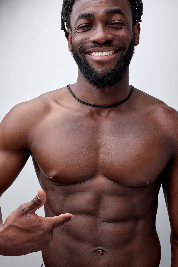 bodybuilder africain souriant positif montrant aux abdos abdominaux, corps musculaire torse nu - Photo, image