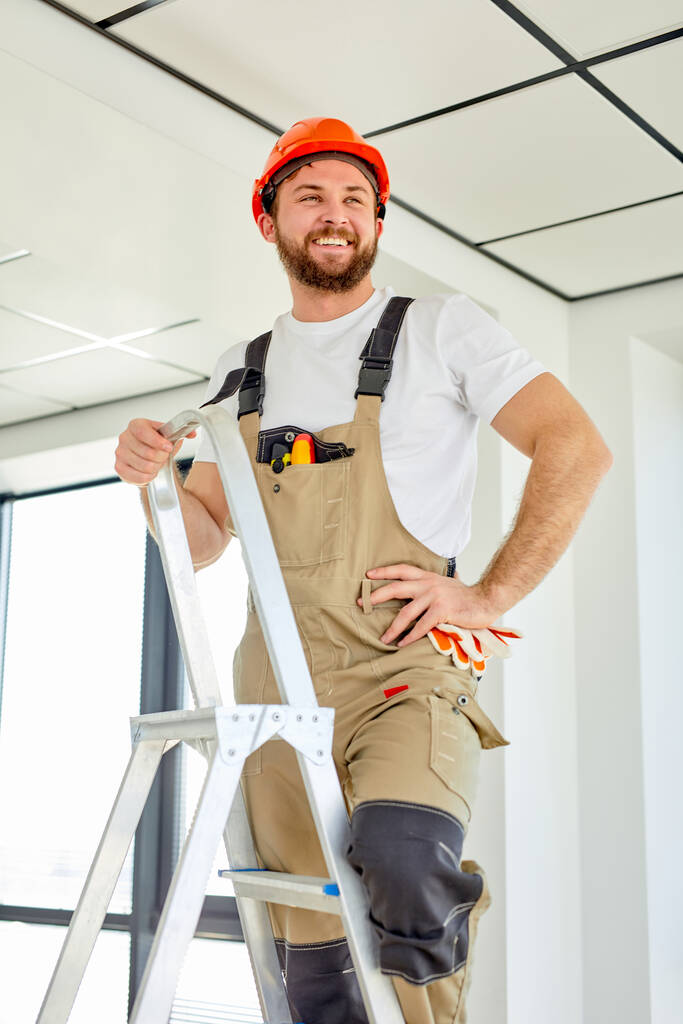 Reparação de quartos. Construtor confiante caucasiano reparar teto, de pé na escada rolante - Foto, Imagem