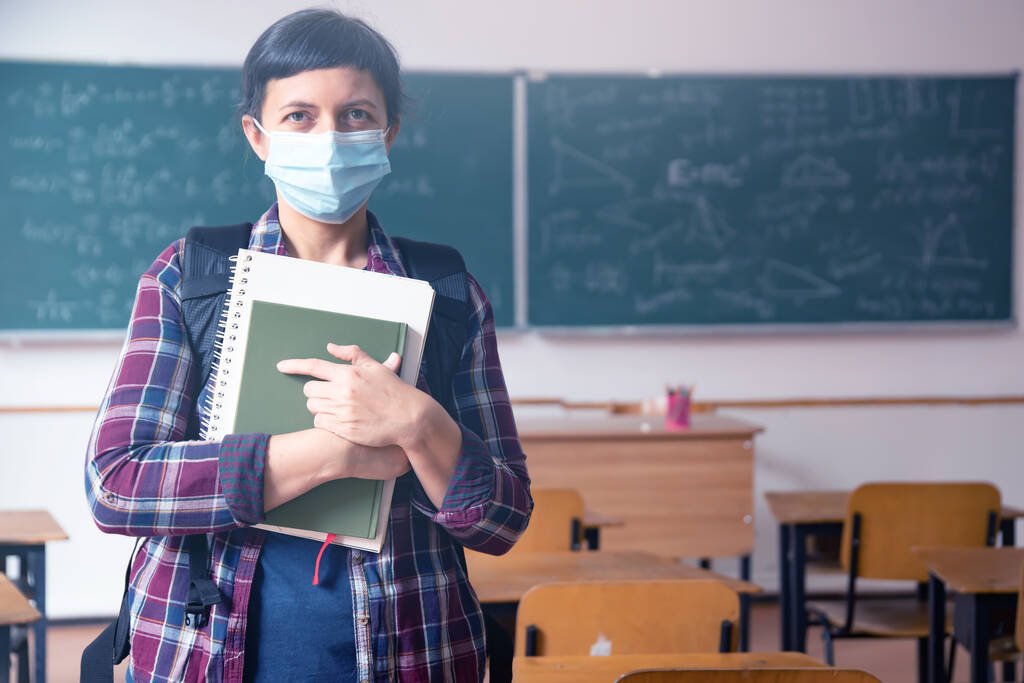 Mosolyogó diáklány iskolatáskában, maszkban és füzetben. Társadalmi távolságtartó és osztálytermi biztonság a koronavírus járvány idején - Fotó, kép