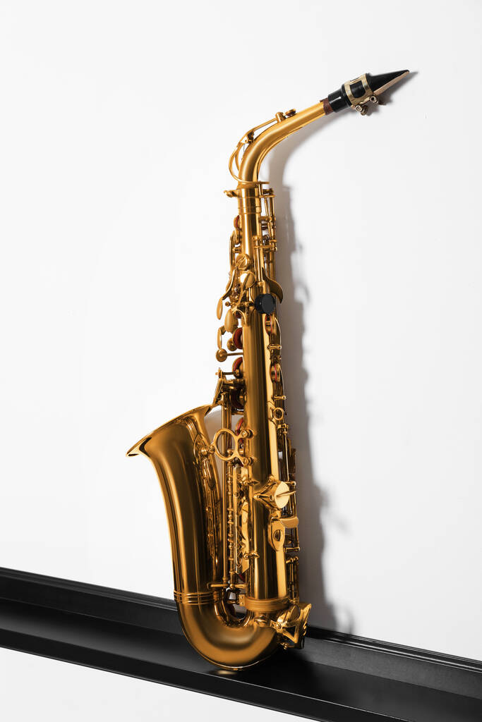 Piękny saksofon na półce przy białej ścianie. Instrument muzyczny - Zdjęcie, obraz
