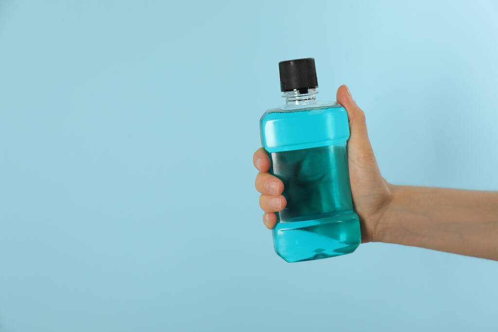 Жінка тримає пляшку з миттям рота на світло-блакитному тлі, крупним планом. Простір для тексту
 - Фото, зображення