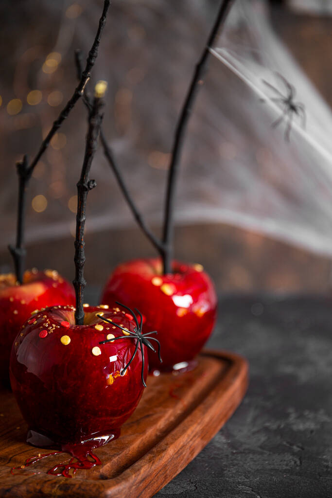  Czerwone jabłka w karmelu z świątecznym wystrojem Halloween, oryginalna uczta na świąteczny stół Halloween ozdobiony pająkami i pajęczynami, zdjęcie pionowe - Zdjęcie, obraz