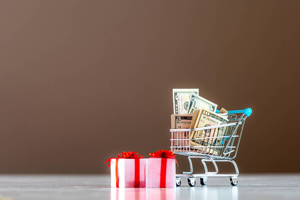 Kerstkostenplanning concept, geschenkdozen en winkelwagentje vol geld - Foto, afbeelding