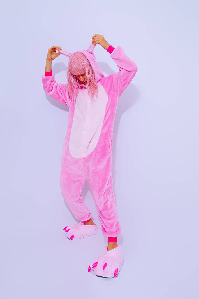 Beyaz stüdyoda poz veren pembe pijamalı parti kızı. Ev Gevşeme tarzı. Kigurumi dükkanı konsepti - Fotoğraf, Görsel