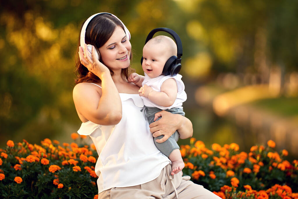 Szczęśliwa kobieta z małym chłopcem w słuchawkach siedzieć w parku. - Zdjęcie, obraz