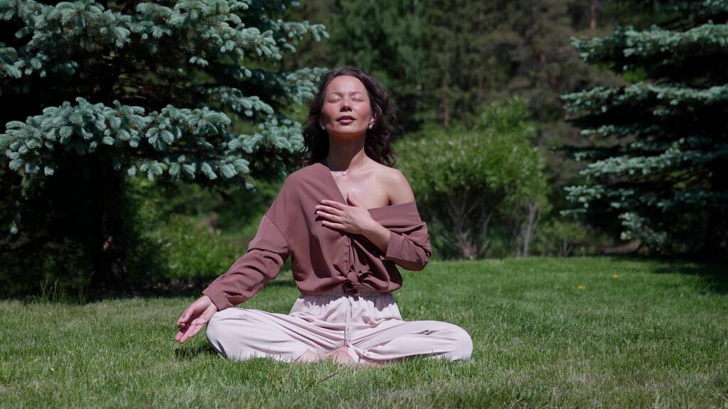 Uma mulher pratica ioga e medita na posição de lótus no parque. Menina saudável sentada na posição de lótus sukhasna, meditando ou praticando ioga na natureza, ao ar livre, relaxante - Foto, Imagem