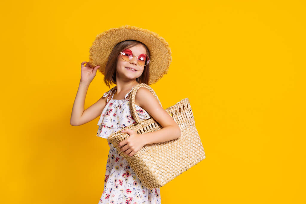 Retrato de menina alegre feliz no chapéu de verão, óculos de sol, saco de palha sobre fundo amarelo.  - Foto, Imagem