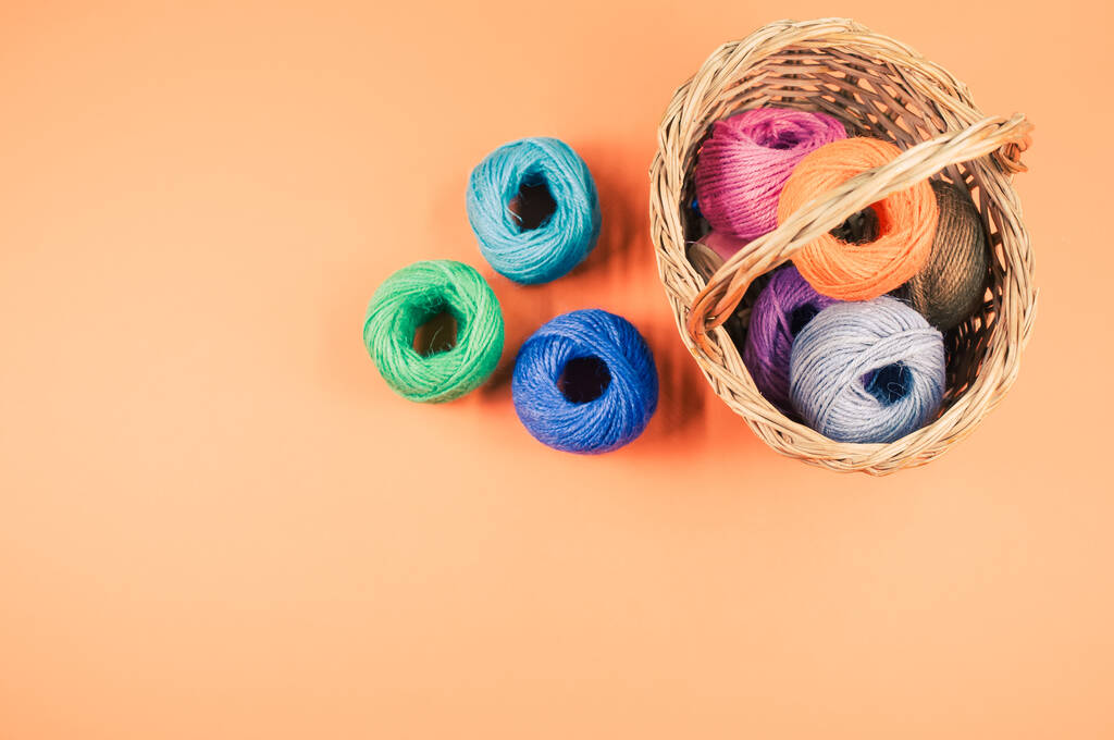 Купка різнокольорових текстильних кульок з вовни у плетеному кошику на помаранчевому фоні з копією простору
 - Фото, зображення