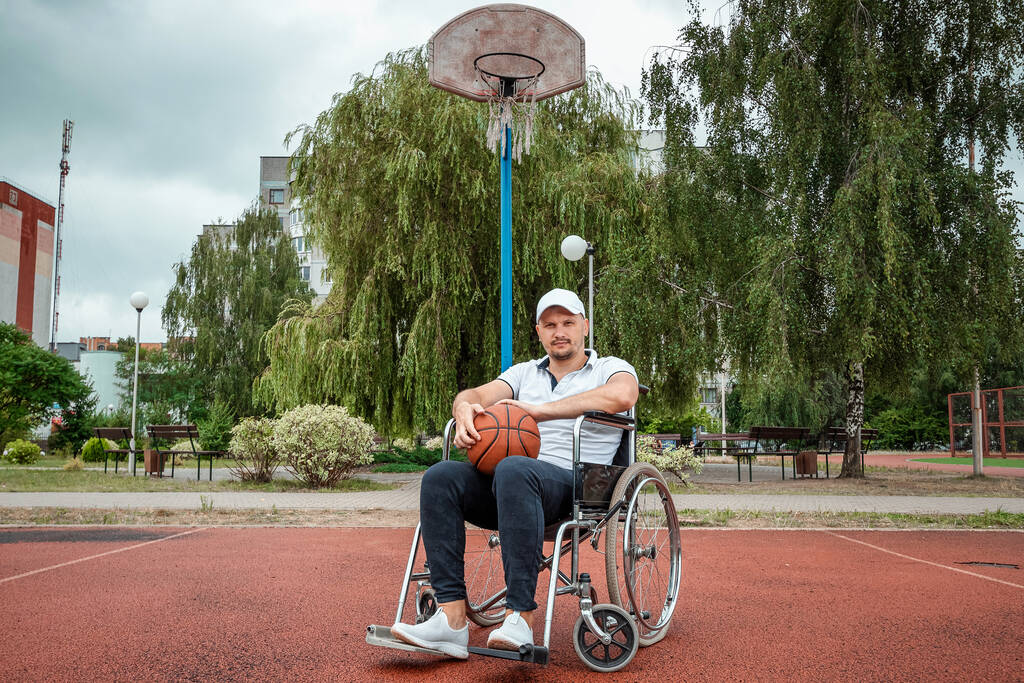 Mężczyzna na wózku gra w kosza na boisku. Koncepcja osoby niepełnosprawnej, satysfakcjonujące życie, osoba niepełnosprawna, sprawność, aktywność, wesołość. - Zdjęcie, obraz