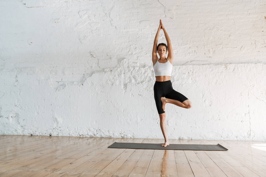 Юная стройная брюнетка фитнес-женщина, растянувшаяся на спортивном коврике в студии - Фото, изображение