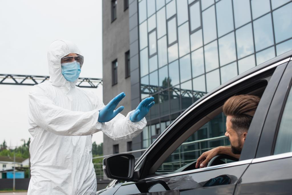 Orvosi dolgozó vegyvédelmi ruhában mutatja stop gesztusok a vezető az autóban  - Fotó, kép