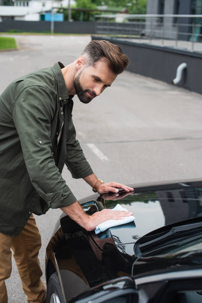 Hombre joven en ropa casual limpiando el coche al aire libre  - Foto, imagen