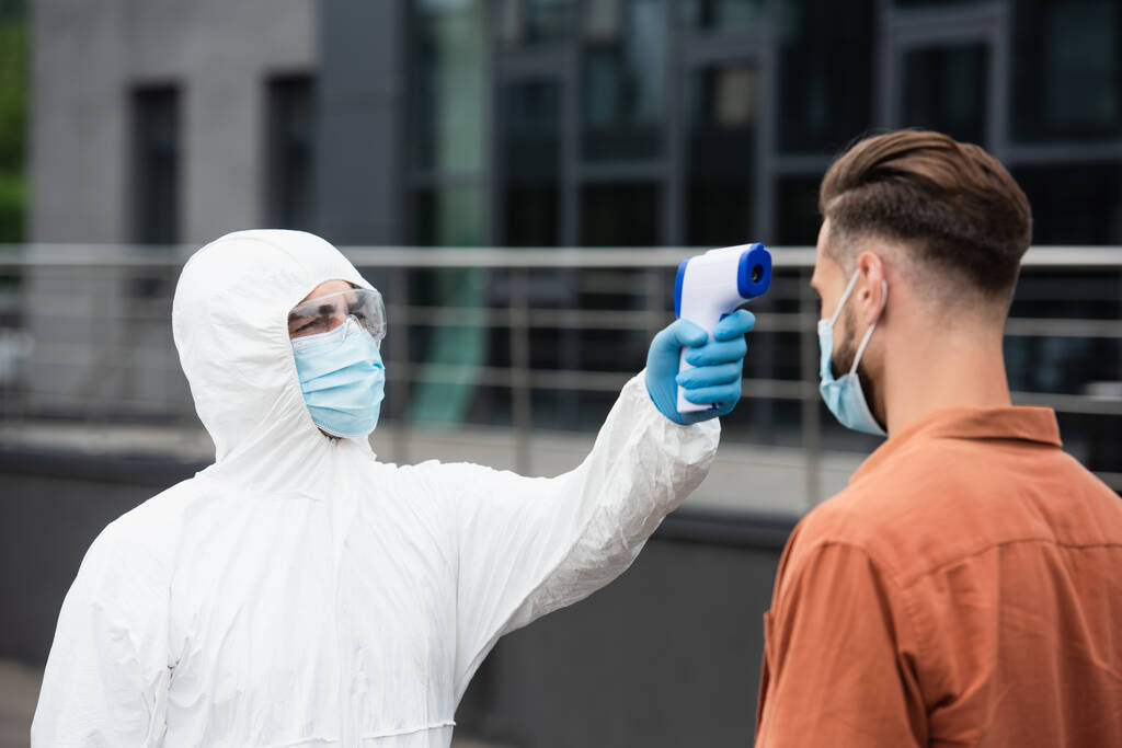 Медичний працівник у костюмі для перевірки температури людини в масці на відкритому повітрі
  - Фото, зображення