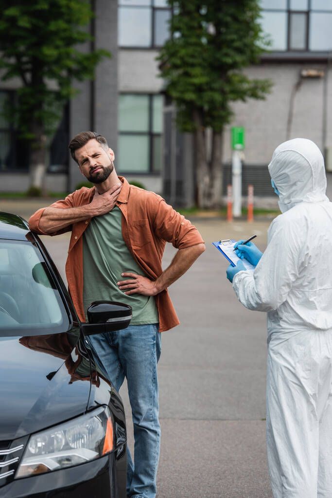 Kranker Fahrer steht neben Auto und Arzt schreibt auf Klemmbrett  - Foto, Bild