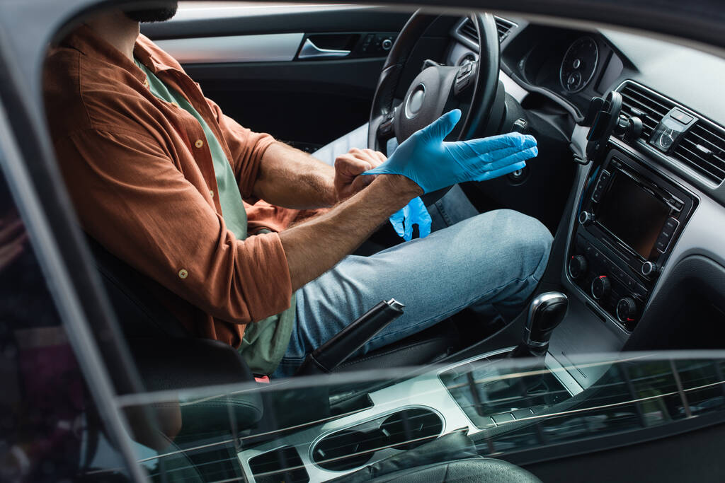 Vista recortada del conductor con guantes de látex en el coche  - Foto, imagen