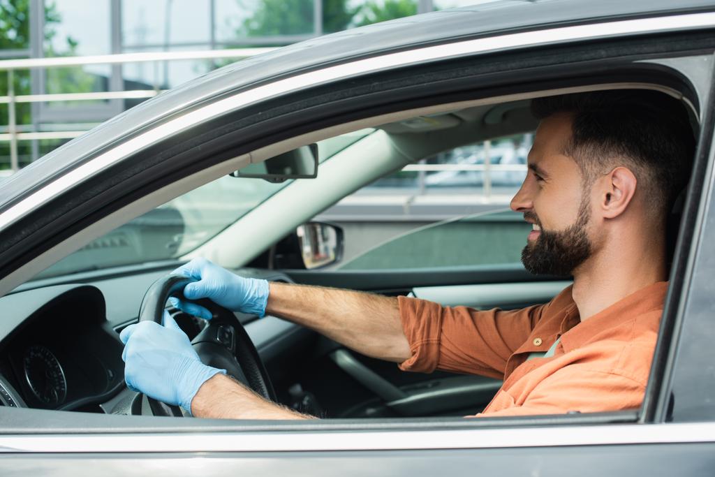Widok z boku uśmiechniętego kierowcy w lateksowych rękawiczkach jazdy samochodem  - Zdjęcie, obraz