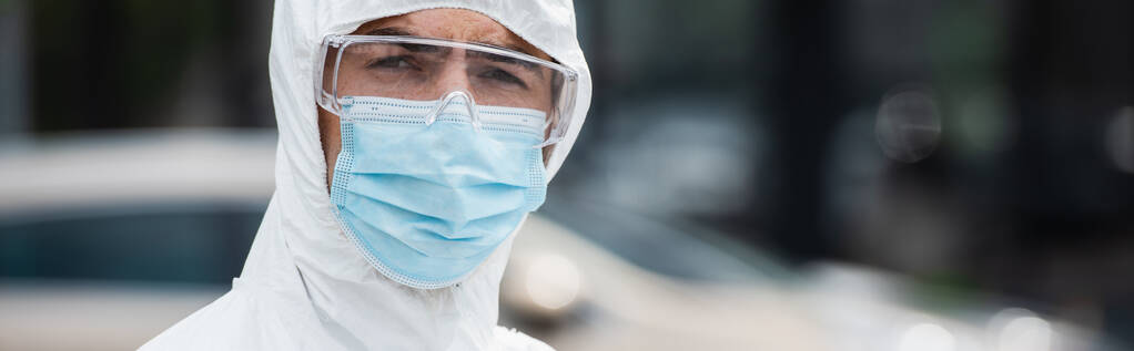 Orvosi munkás védő maszkban és védőszemüvegben a szabadban lévő kamerát nézi, transzparens  - Fotó, kép