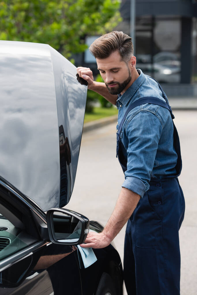 Mechanic in overalls wiping car outdoors  - Photo, Image