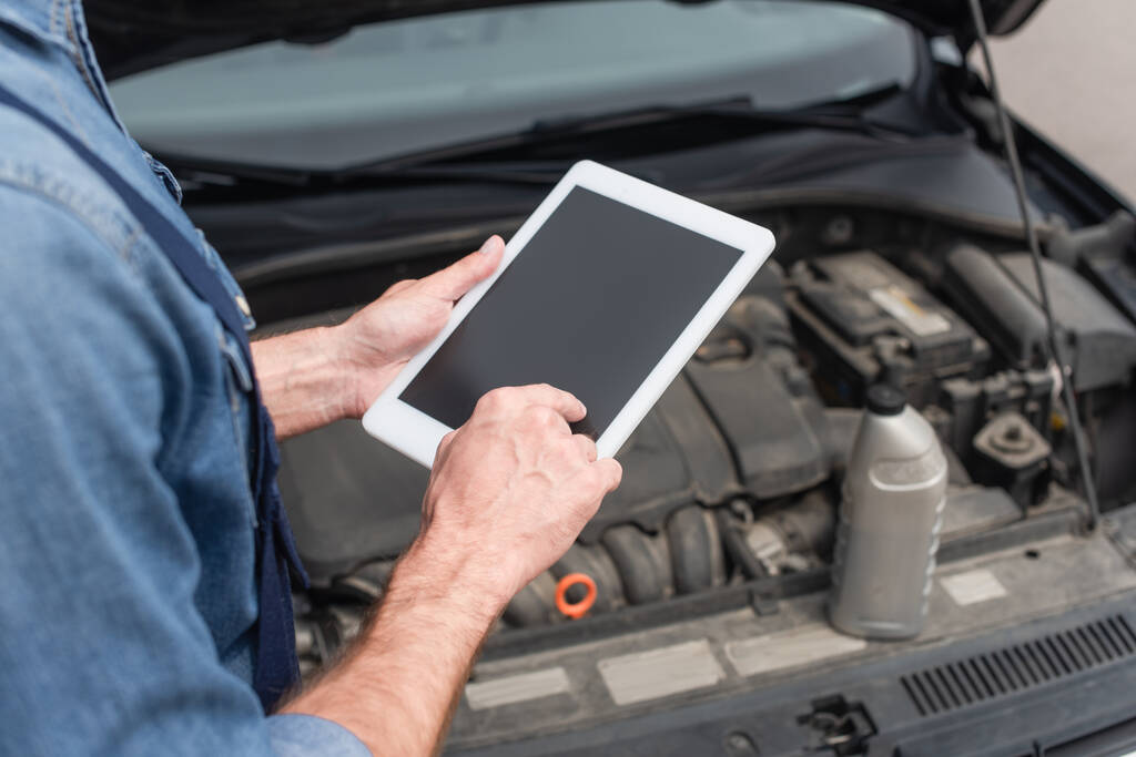 Rajatut näkymä mekaanikko käyttäen digitaalista tabletti lähellä hämärtynyt auto  - Valokuva, kuva