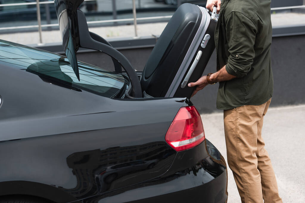 Cropped view of man putting suitcase in car trunk outdoors  - Photo, Image
