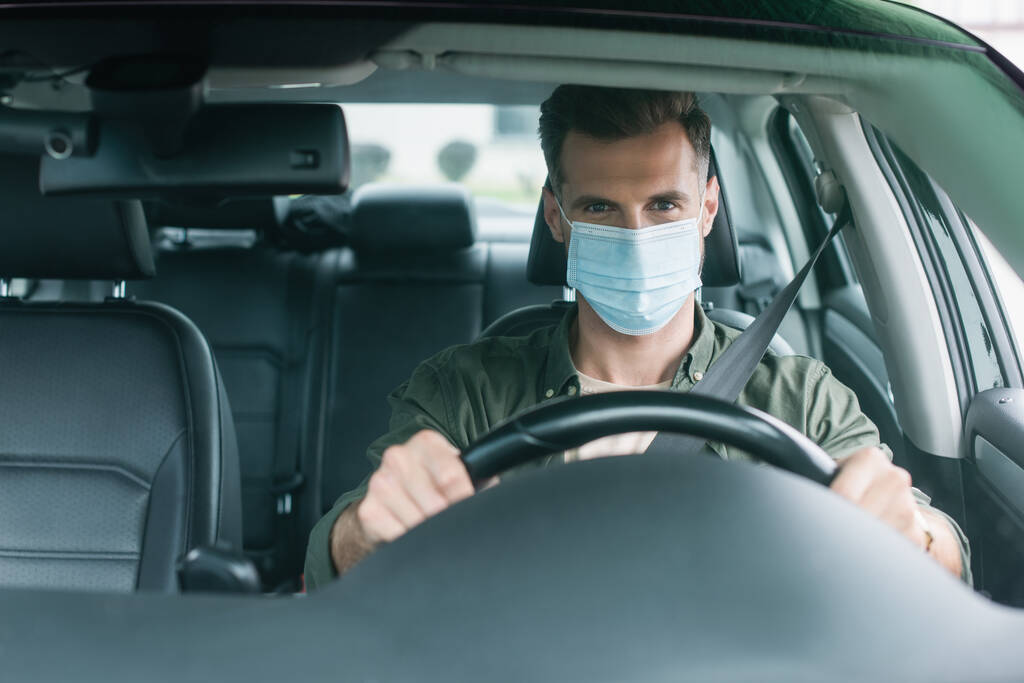 Sofőr orvosi maszkban nézi a kamerát autóban  - Fotó, kép