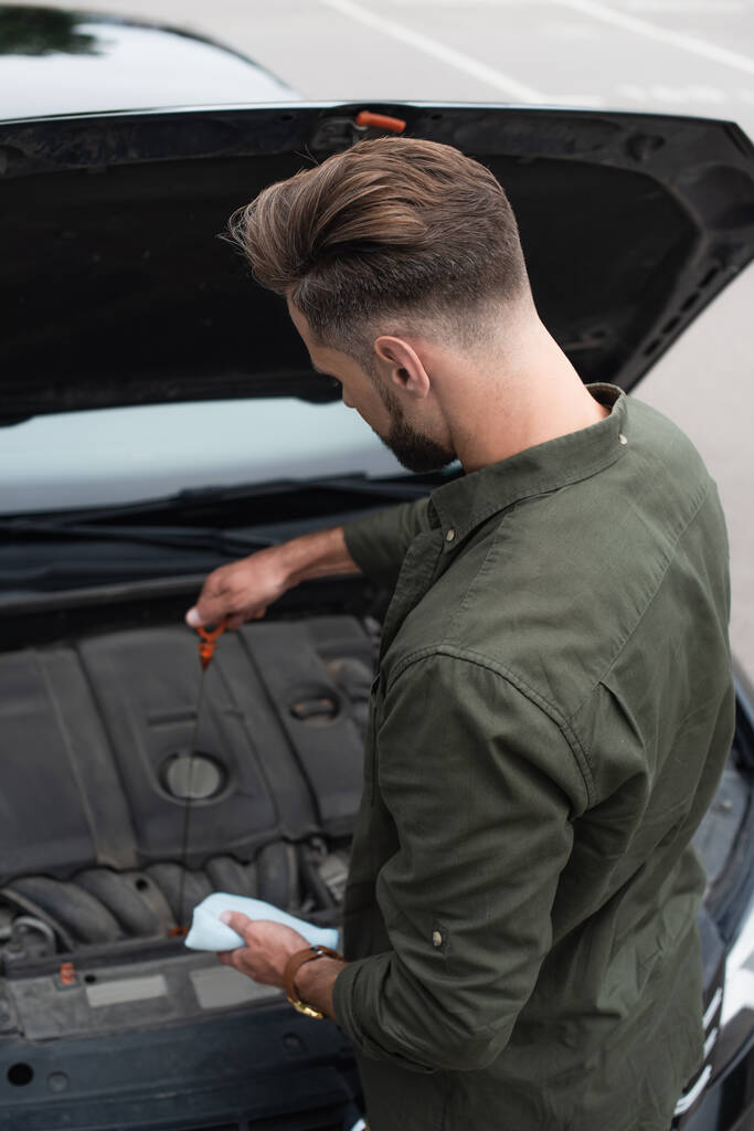 Водитель с тряпкой проверяет масло в двигателе автомобиля  - Фото, изображение
