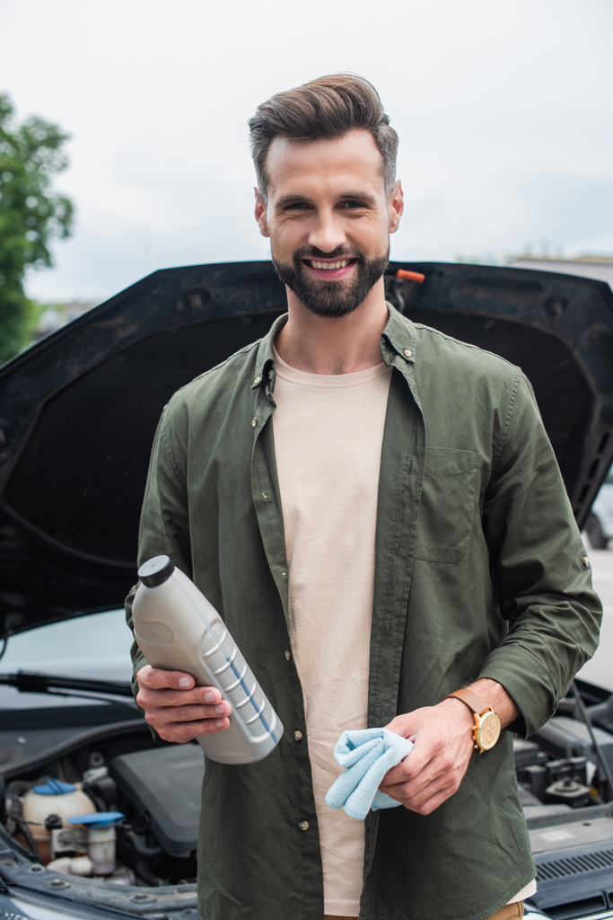 Usmívající se řidič drží hadr a motorový olej v blízkosti rozmazané auto  - Fotografie, Obrázek