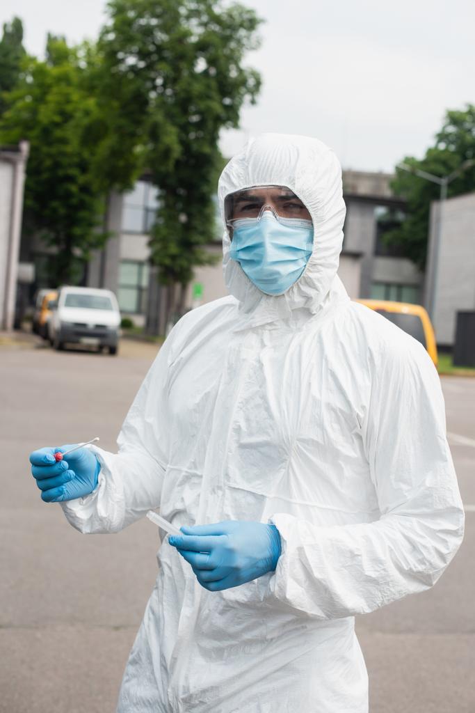 Orvosi dolgozó vegyvédelmi ruhában tartja pcr teszt szabadban  - Fotó, kép