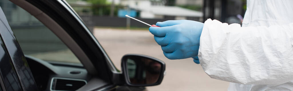 Gewassen beeld van medisch werker in hazmat pak houden pcr test in de buurt van auto, banner  - Foto, afbeelding