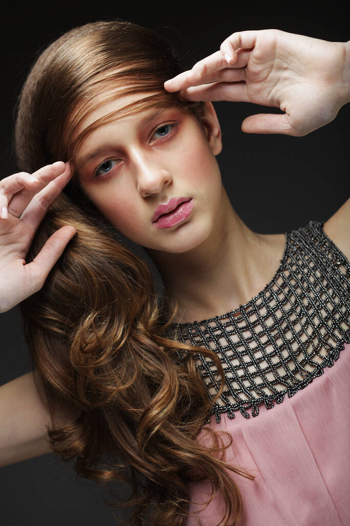 Schöne Frau mit Make-up in rosa Tönen. Mädchen-Modell mit geflochtenem Zopf auf schwarzem Hintergrund. Frisur liegt im Trend. Schönheit, Mode, Kosmetik und Kosmetik. - Foto, Bild
