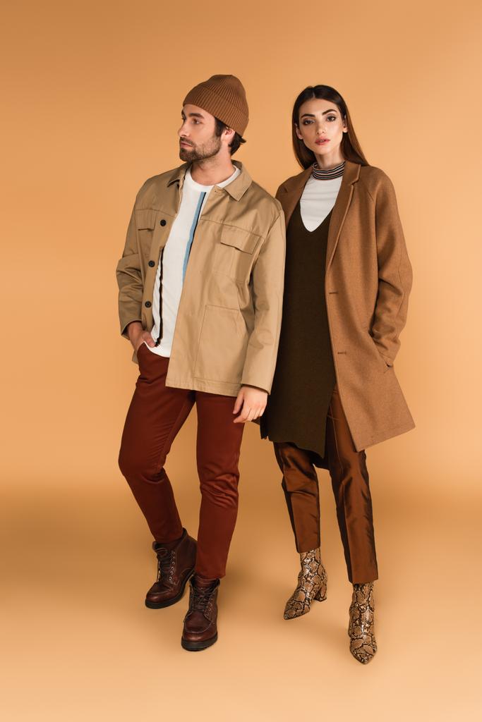full length view of couple in trendy autumn clothes standing on beige background - Foto, imagen
